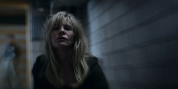 Movie still from “Awake” (2021), directed by Mark Raso – A woman with long blonde hair is standing by a brick wall; Close Up shot, Low angle