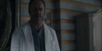 Movie still from “Awake” (2021), directed by Mark Raso – A man wearing a lab coat standing next to a wall; Medium shot, Low angle