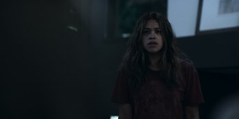 Movie still from “Awake” (2021), directed by Mark Raso – A young woman with long hair standing in front of a building; Medium shot, Low angle