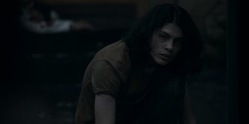 Movie still from “Awake” (2021), directed by Mark Raso – A person with long hair is standing in a dark room; Medium shot, High angle