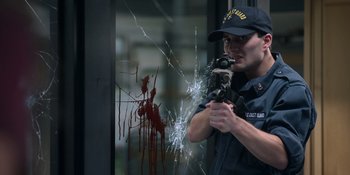 Movie still from “Awake” (2021), directed by Mark Raso – A police officer holding a gun in front of a shattered window; Medium shot, Low angle