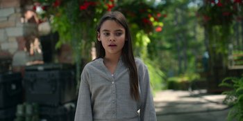 Movie still from “Awake” (2021), directed by Mark Raso – A young girl in a gray shirt is standing in front of a tree; Medium shot, High angle