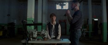 Movie still from “Baby Driver” (2017), directed by Edgar Wright – A man sitting at a table in a room with another man; Medium shot, Over the shoulder angle