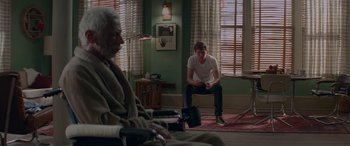 Movie still from “Baby Driver” (2017), directed by Edgar Wright – A man sitting on the ground in a living room next to an older man; Wide shot, Over the shoulder angle