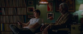 Movie still from “Baby Driver” (2017), directed by Edgar Wright – Two people sitting in a room with a lamp on the wall behind them; Medium shot, Over the shoulder angle