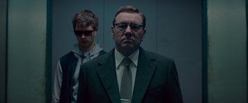 Movie still from “Baby Driver” (2017), directed by Edgar Wright – A man in a suit and tie standing next to a man in glasses; Close Up shot, Low angle