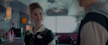 Movie still from “Baby Driver” (2017), directed by Edgar Wright – A woman in a black and white uniform standing in front of red seats in a room; Close Up shot, Over the shoulder angle