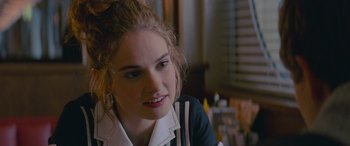 Movie still from “Baby Driver” (2017), directed by Edgar Wright – A young woman sitting at a table looking at the camera; Close Up shot, Over the shoulder angle