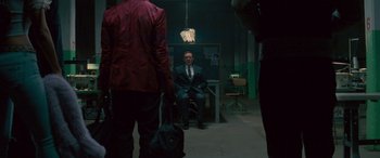 Movie still from “Baby Driver” (2017), directed by Edgar Wright – A man in a suit sitting on a bench in a dark room; Wide shot, Over the shoulder angle