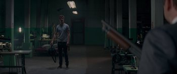Movie still from “Baby Driver” (2017), directed by Edgar Wright – A man standing in a room holding a gun; Wide shot, Over the shoulder angle