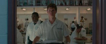 Movie still from “Baby Driver” (2017), directed by Edgar Wright – A young man in a white shirt is standing in front of other people; Close Up shot, Over the shoulder angle
