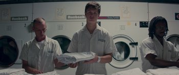 Movie still from “Baby Driver” (2017), directed by Edgar Wright – A young man holding a white shirt in a laundry room; Medium shot, Low angle
