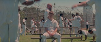 Movie still from “Baby Driver” (2017), directed by Edgar Wright – A man sitting on top of a wooden bench in a field; Wide shot, High angle