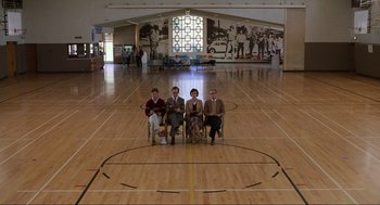 Movie still from “Back to the Future” (1985), directed by Robert Zemeckis – A group of people sitting on chairs in a gymnasium; Extreme Wide shot, High angle