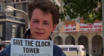 Movie still from “Back to the Future” (1985), directed by Robert Zemeckis – A young man holding a sign that says " the clock tower "; Close Up shot, Low angle