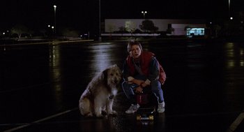 Movie still from “Back to the Future” (1985), directed by Robert Zemeckis – A person and a dog sitting in a parking lot at night; Wide shot, Low angle