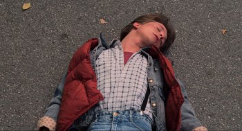 Movie still from “Back to the Future” (1985), directed by Robert Zemeckis – A person laying on the ground with their eyes closed; Medium shot, Overhead angle