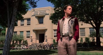 Movie still from “Back to the Future” (1985), directed by Robert Zemeckis – A man standing in front of a building with bicycles parked in front of it; Wide shot, Low angle