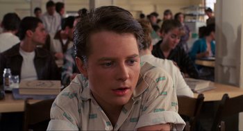 Movie still from “Back to the Future” (1985), directed by Robert Zemeckis – A young man sitting at a table with a bunch of other people; Close Up shot, Over the shoulder angle