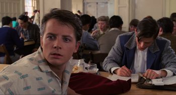 Movie still from “Back to the Future” (1985), directed by Robert Zemeckis – A man sitting at a table in front of other people; Medium shot, Over the shoulder angle