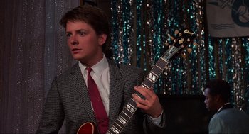 Movie still from “Back to the Future” (1985), directed by Robert Zemeckis – A man in a suit and tie holding an electric guitar; Medium shot, Over the shoulder angle