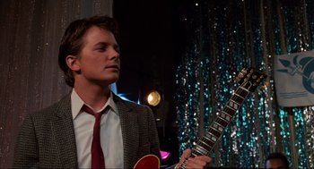 Movie still from “Back to the Future” (1985), directed by Robert Zemeckis – A man in a suit and tie holding a guitar; Medium shot, Over the shoulder angle