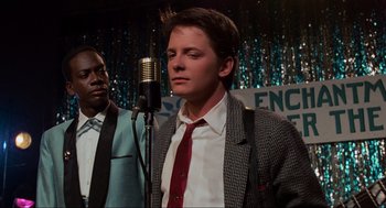 Movie still from “Back to the Future” (1985), directed by Robert Zemeckis – A man in a suit and tie standing in front of a microphone; Close Up shot, Over the shoulder angle