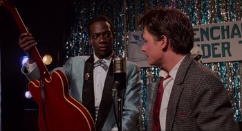 Movie still from “Back to the Future” (1985), directed by Robert Zemeckis – Two men in suits and ties with a microphone and a guitar; Medium shot, Over the shoulder angle