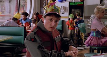 Movie still from “Back to the Future Part II” (1989), directed by Robert Zemeckis – A man wearing a party hat in front of a group of people; Medium shot, Over the shoulder angle