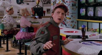 Movie still from “Back to the Future Part II” (1989), directed by Robert Zemeckis – A man in a red and gray jacket and a red hat is standing in front of a table; Close Up shot, Over the shoulder angle