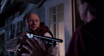 Movie still from “Back to the Future Part II” (1989), directed by Robert Zemeckis – A man holding a gun while standing in front of a building; Close Up shot, Over the shoulder angle