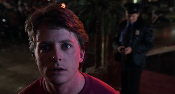 Movie still from “Back to the Future Part II” (1989), directed by Robert Zemeckis – A young man stares into the camera while a security guard watches; Close Up shot, Over the shoulder angle