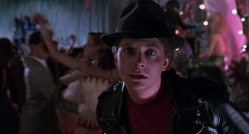 Movie still from “Back to the Future Part II” (1989), directed by Robert Zemeckis – A young man wearing a black hat in front of a group of people; Close Up shot, Over the shoulder angle