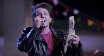 Movie still from “Back to the Future Part II” (1989), directed by Robert Zemeckis – A man in a black leather jacket holding a newspaper; Medium shot, Low angle