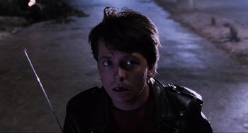 Movie still from “Back to the Future Part II” (1989), directed by Robert Zemeckis – A man with a leather jacket and a red shirt is looking at the camera; Close Up shot, Over the shoulder angle