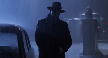 Movie still from “Back to the Future Part II” (1989), directed by Robert Zemeckis – A man wearing a hat standing next to a car in the rain; Medium shot, Low angle