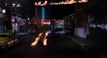 Movie still from “Back to the Future Part II” (1989), directed by Robert Zemeckis – A woman walking down the street with a fire in her hand; Extreme Wide shot, High angle
