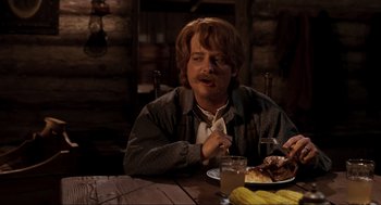 Movie still from “Back to the Future Part III” (1990), directed by Robert Zemeckis – A man sitting at a wooden table eating food; Medium shot, Over the shoulder angle