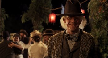 Movie still from “Back to the Future Part III” (1990), directed by Robert Zemeckis – A man in a hat and a suit and tie smiling; Medium shot, Over the shoulder angle