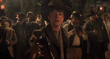 Movie still from “Back to the Future Part III” (1990), directed by Robert Zemeckis – A man in a hat holding a gun in front of a group of people; Medium shot, Over the shoulder angle