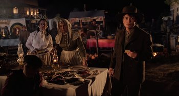 Movie still from “Back to the Future Part III” (1990), directed by Robert Zemeckis – A group of people standing around a table with plates of food on top of it; Medium shot, Over the shoulder angle