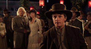 Movie still from “Back to the Future Part III” (1990), directed by Robert Zemeckis – A man in a hat standing in front of a group of people; Close Up shot, Over the shoulder angle