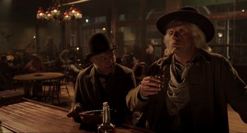 Movie still from “Back to the Future Part III” (1990), directed by Robert Zemeckis – Two men sitting at a table with a glass of beer; Medium shot, Low angle