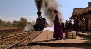 Movie still from “Back to the Future Part III” (1990), directed by Robert Zemeckis – A woman in a purple dress standing next to a train; Wide shot, Low angle