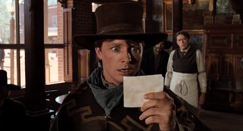 Movie still from “Back to the Future Part III” (1990), directed by Robert Zemeckis – A man holding a piece of paper in front of a group of people; Close Up shot, Over the shoulder angle