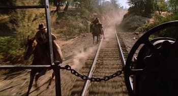 Movie still from “Back to the Future Part III” (1990), directed by Robert Zemeckis – Two men on horseback riding along a train track; Wide shot, Low angle