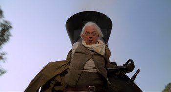 Movie still from “Back to the Future Part III” (1990), directed by Robert Zemeckis – An old man with a white beard is sitting in a chair; Medium shot, Low angle