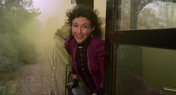 Movie still from “Back to the Future Part III” (1990), directed by Robert Zemeckis – A woman in a purple jacket leaning against a wall; Medium shot, Low angle