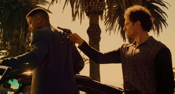 Movie still from “Bad Boys” (1995), directed by Michael Bay – A man holding a gun while standing next to a palm tree; Medium shot, Over the shoulder angle
