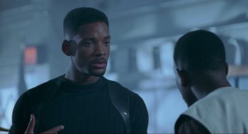 Movie still from “Bad Boys” (1995), directed by Michael Bay – A man standing next to another man in a room; Medium shot, Over the shoulder angle